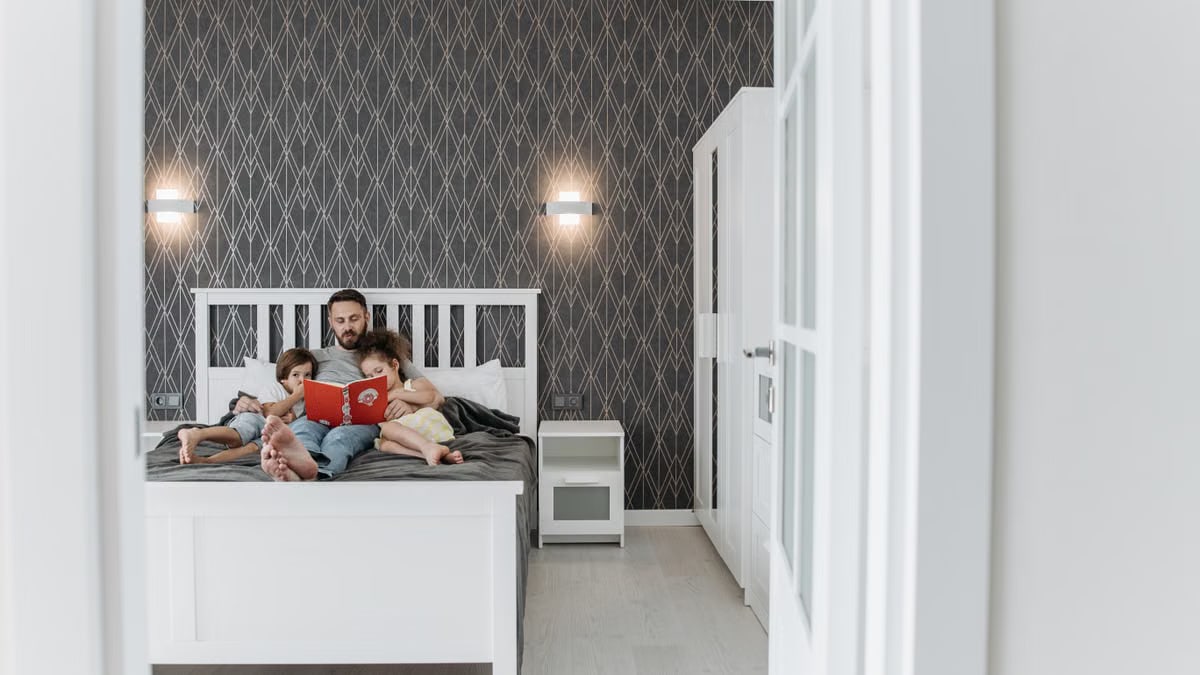 Father and children enjoy a bonding storytime in a cozy, modern bedroom setting.