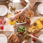 Aerial shot of a diverse brunch spread on a table with multiple hands serving food.