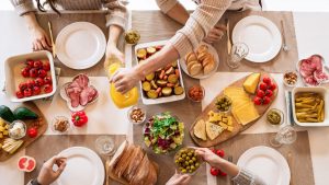 Aerial shot of a diverse brunch spread on a table with multiple hands serving food.